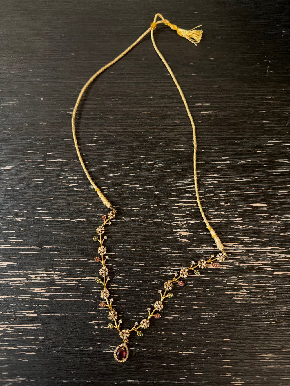The original phone photo: a gold vine necklace with a red pendant on a dark wooden table